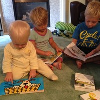 Three very young children (ages 1–5) sitting on a living room floor looking at books